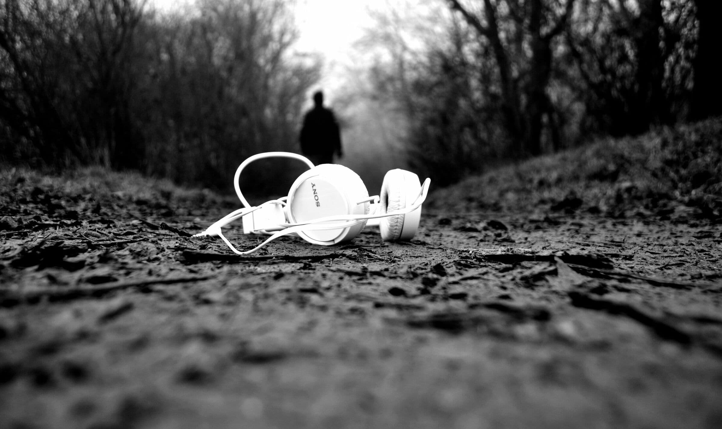 Weiße Kopfhörer liegen auf einem Waldweg, schwarzweiß